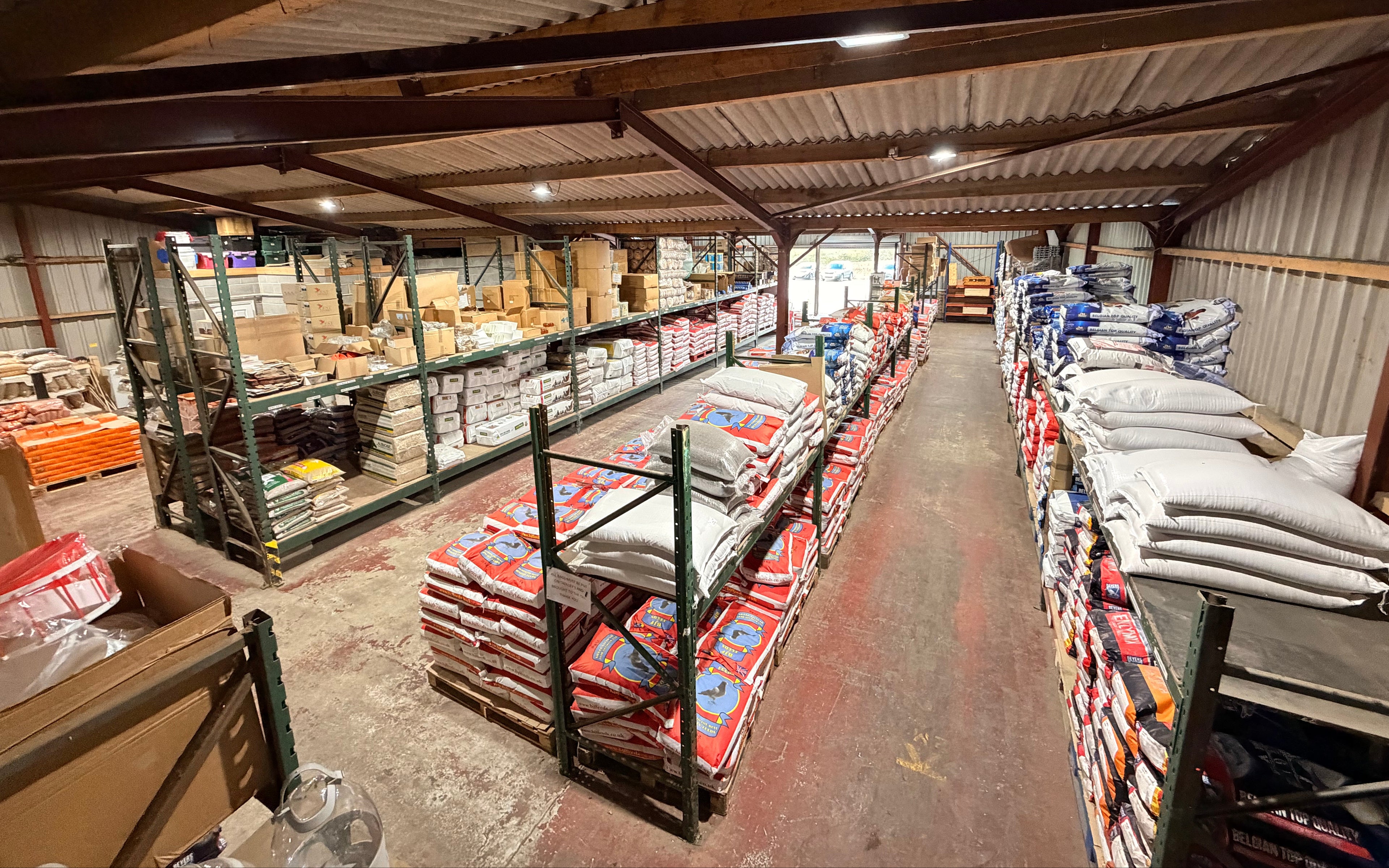 Storage warehouse with shelves and pallets filled with bags and boxes.
